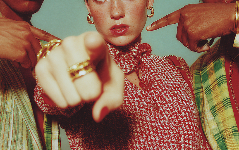 A woman in red points directly at the camera as others around her point toward her — a symbolic image of how individuals confront themselves amid the gaze and judgment of others.