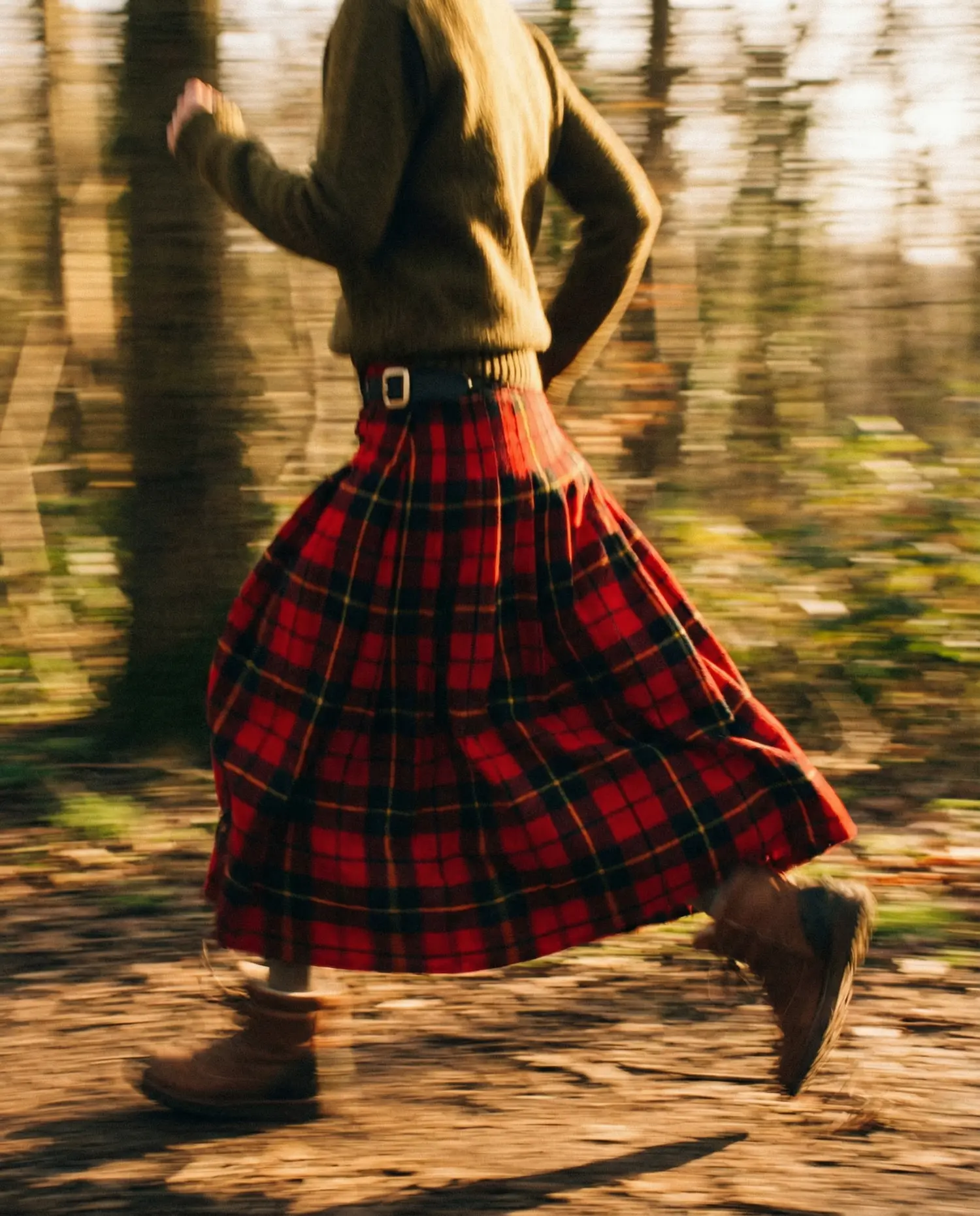 A person running through a sunlit forest wearing a flowing red tartan skirt, capturing a rustic, Scottish-inspired mood