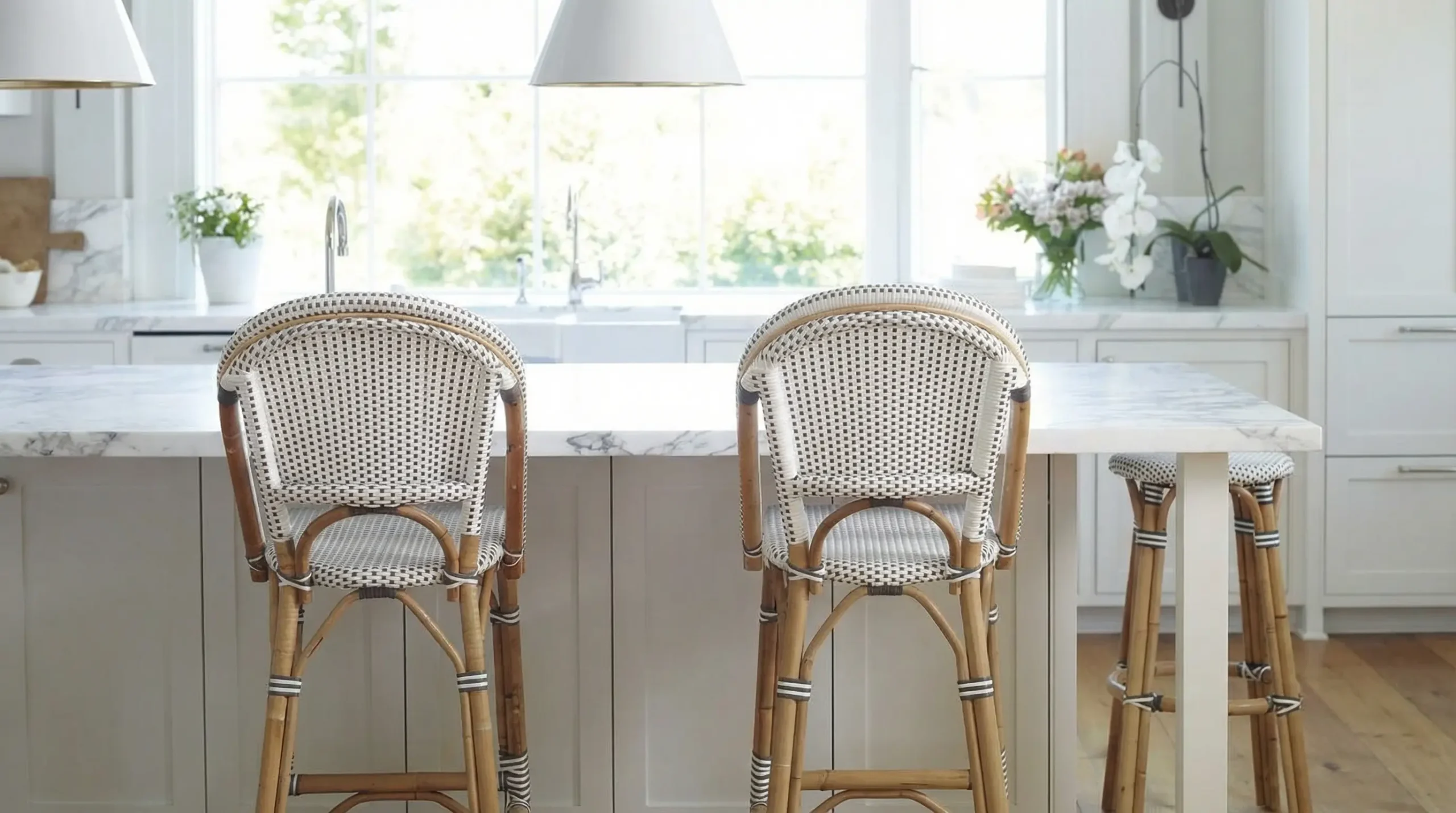 Two light-check–pattern rattan bar stools placed at a white kitchen island, surrounded by soft natural light