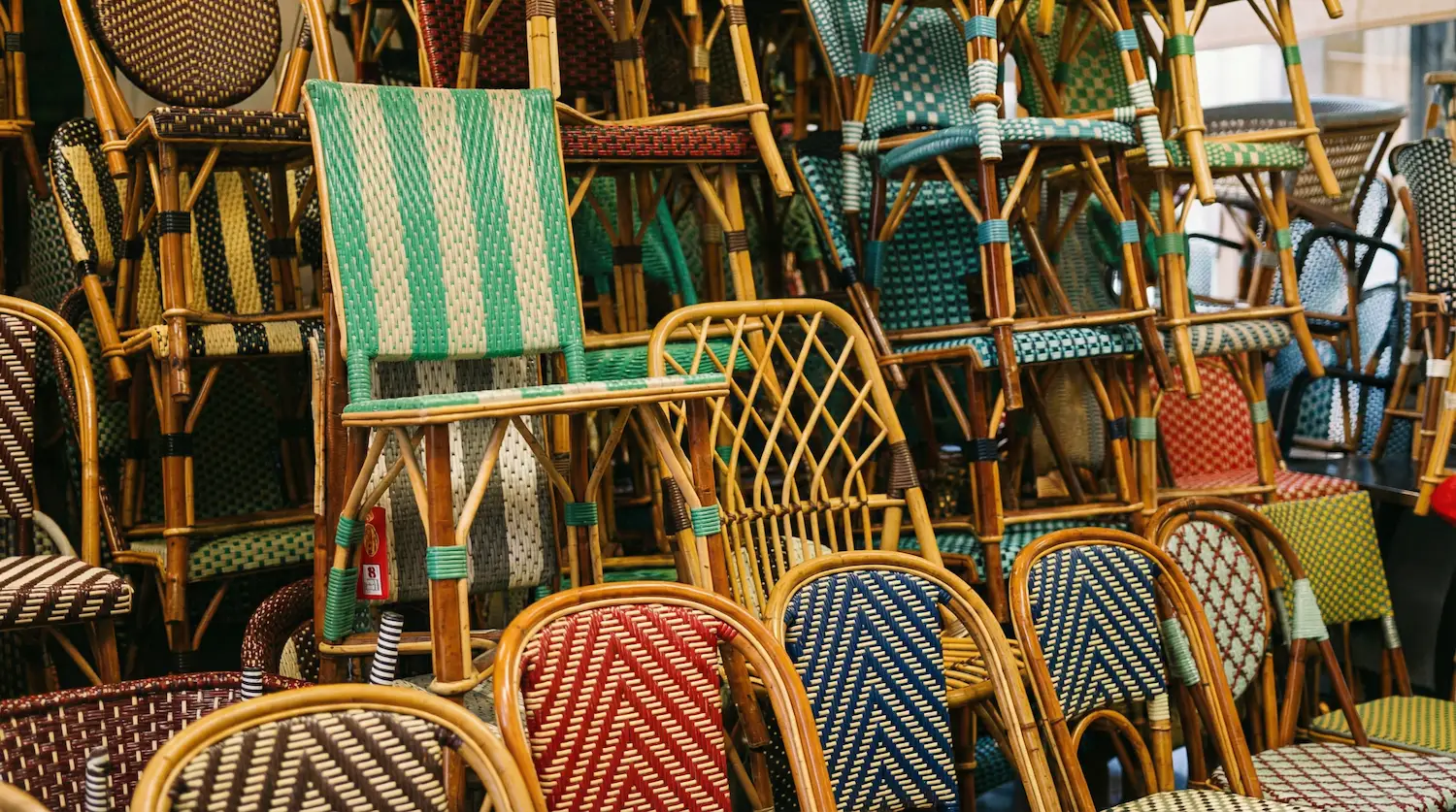 A dense display of rattan bistro chairs featuring various woven patterns—check, zigzag, and geometric—stacked inside an artisan workshop